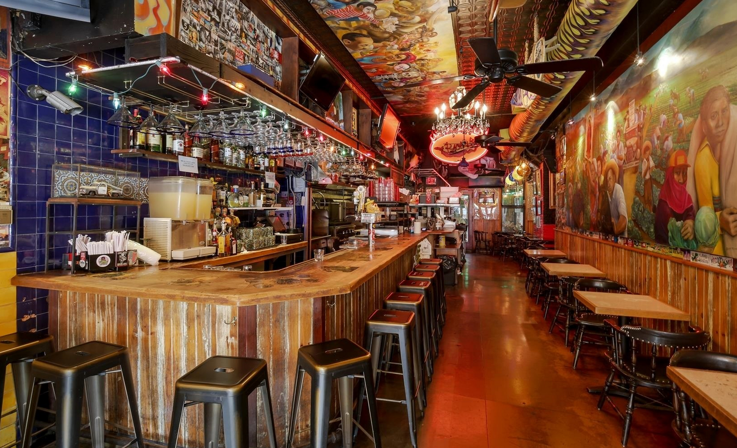 Bar interior with a wooden counter and stools, colorful mural on the wall, and tables.