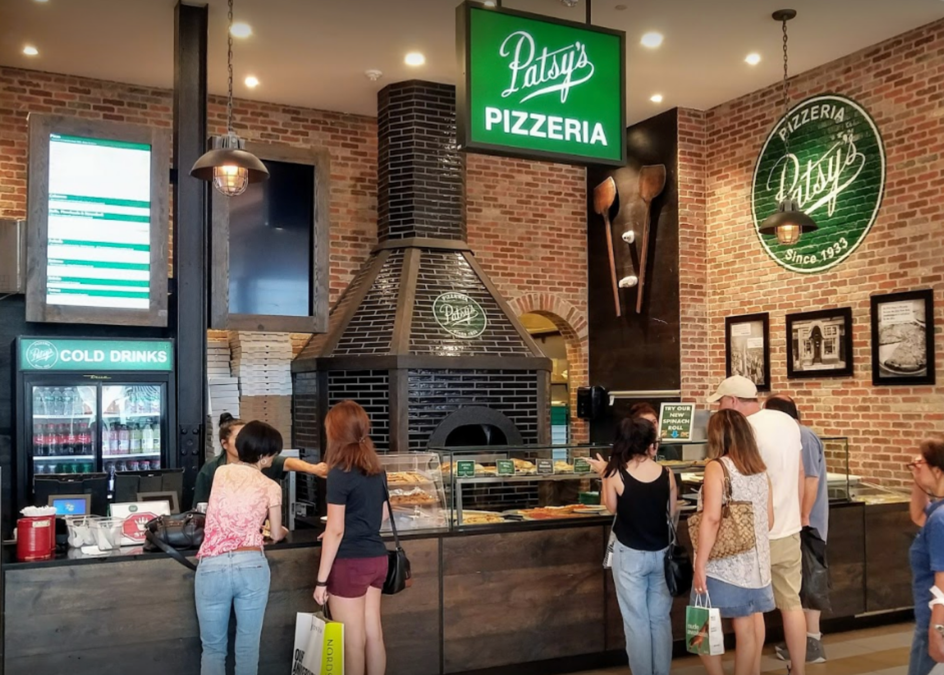 Inside Patsy's Pizzeria: Customers ordering food at the counter. A large brick oven is central.