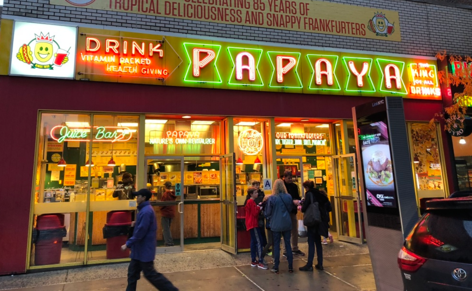 Exterior of a Drink Papaya store with neon sign and customers in front of the entrance.