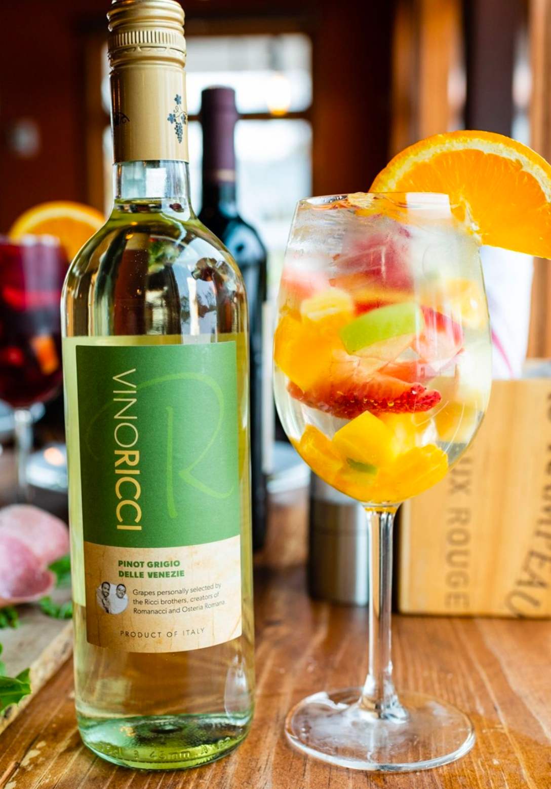 Bottle of Vinoricci white wine next to a glass of fruit sangria garnished with orange slice.