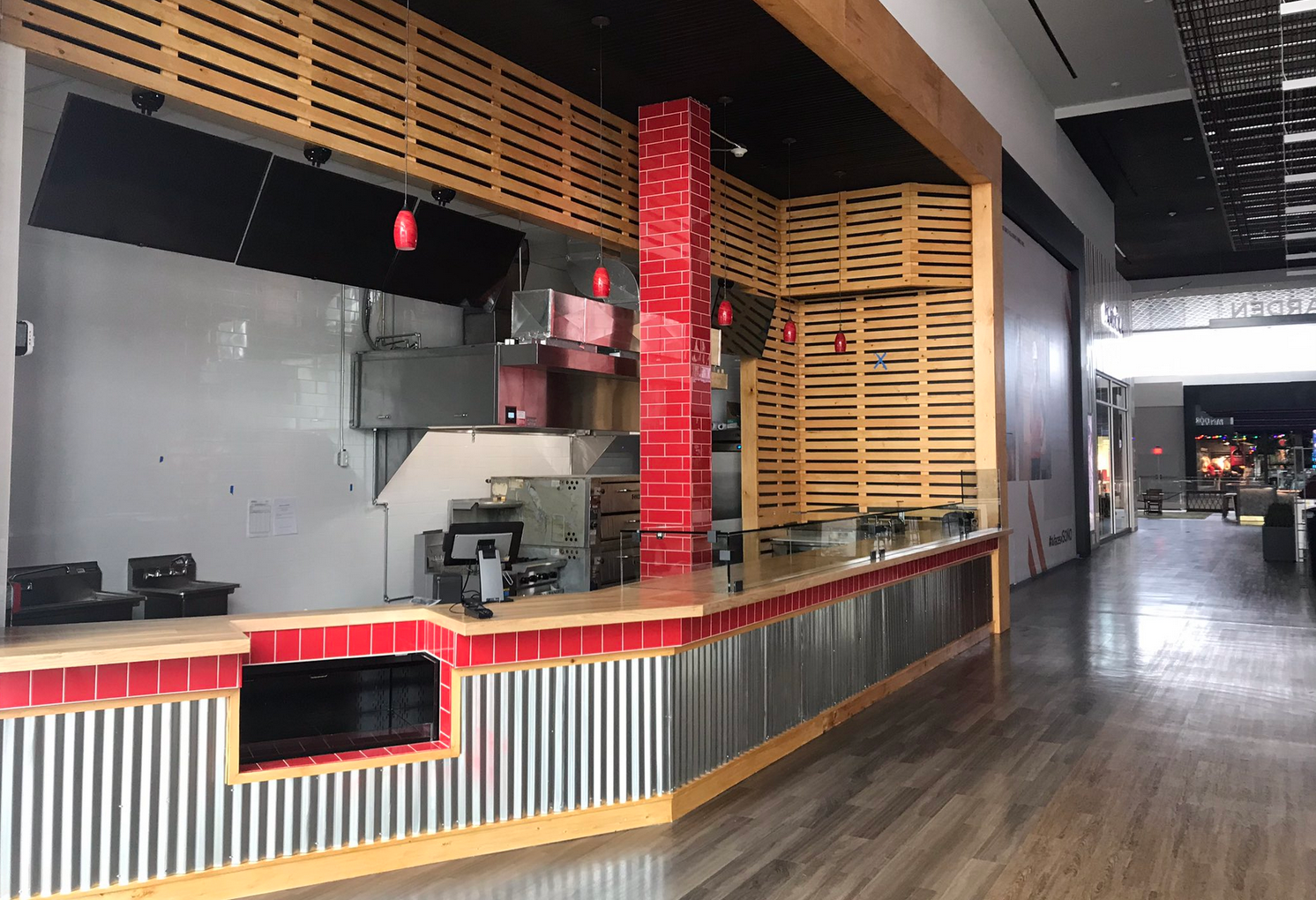 Empty food stall in a mall, red and wood accents, corrugated metal base, equipment visible.