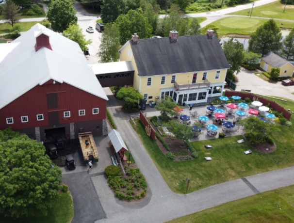 Aerial view of a yellow house with an attached barn and outdoor dining with colorful umbrellas.