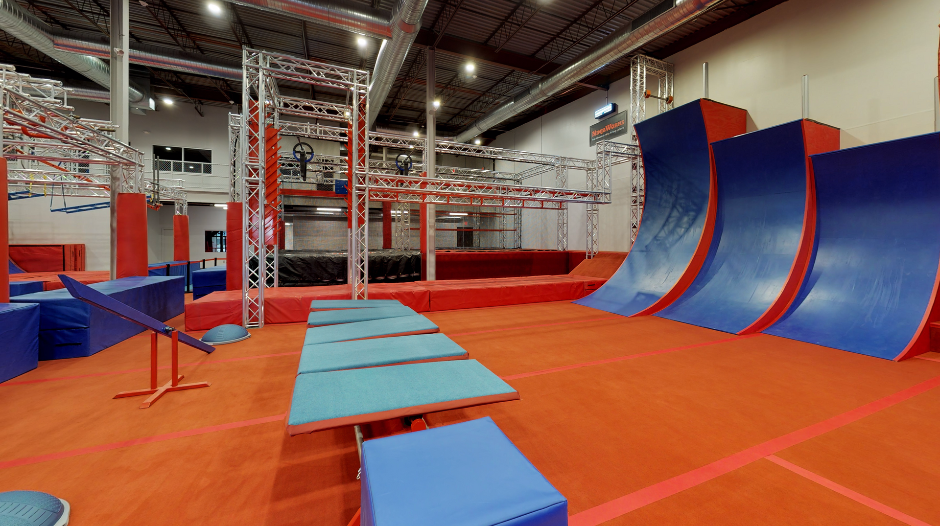 Indoor ninja warrior gym with obstacles, including angled walls and balance beams.