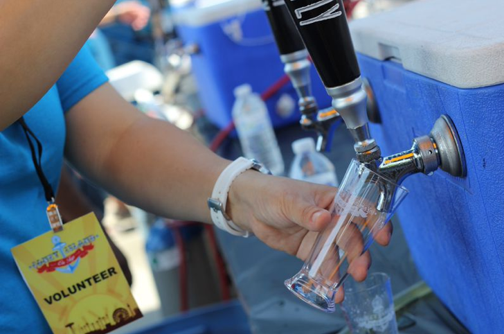 Person pouring beer from a tap into a glass. Volunteer badge visible.
