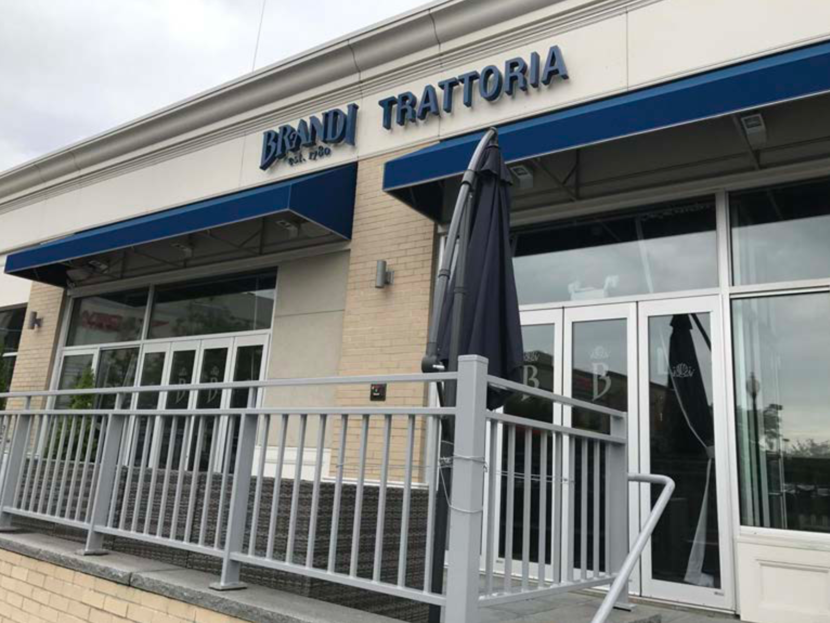 Brandi Trattoria restaurant exterior with blue awning, glass doors, and a metal railing.