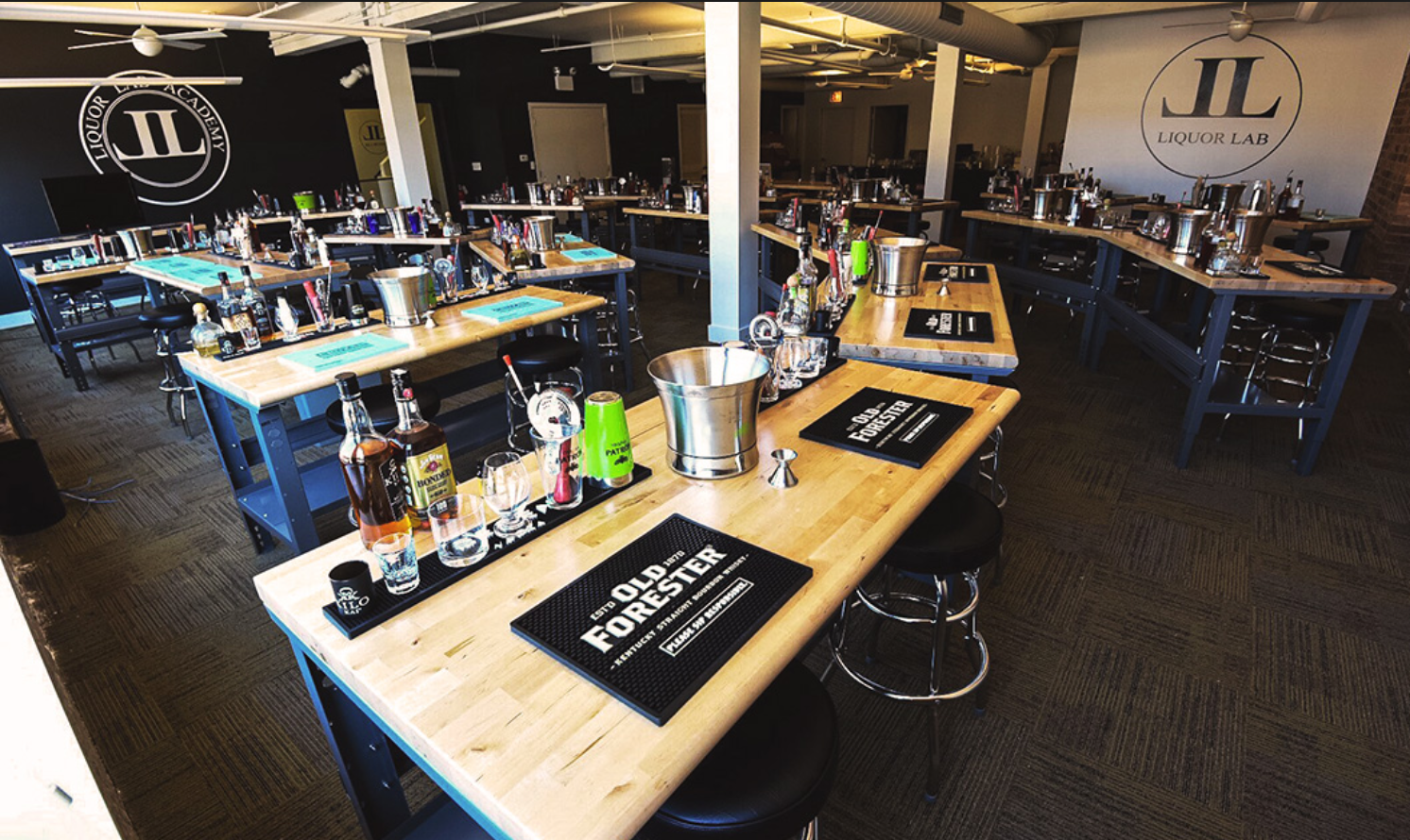 Cocktail class setup: bar workstations with liquor bottles, shakers, ice buckets, and bar tools.
