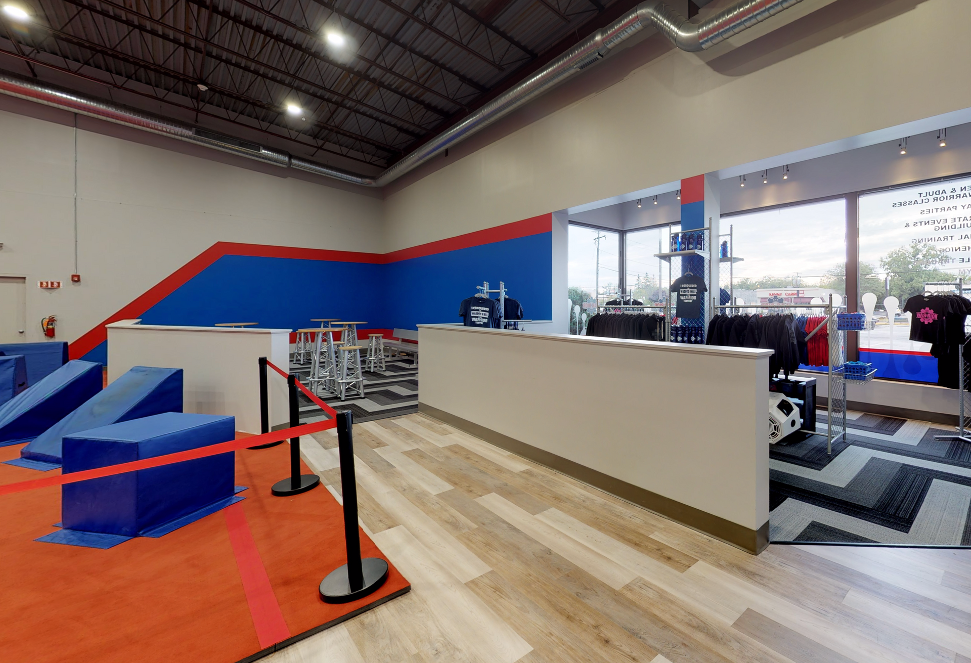 Interior of a gym with a reception desk, obstacle course, and seating area. Red, blue, and white color scheme.