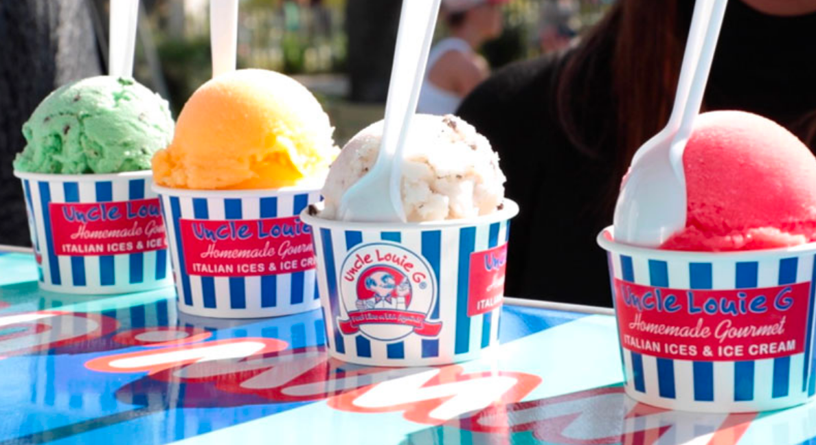 Four cups of colorful Italian ice and ice cream with spoons, sitting on a blue and white striped table.