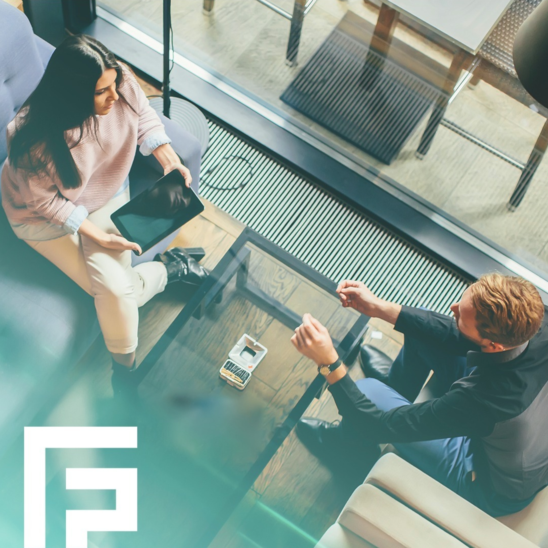 Two people in a modern office space, sitting and interacting over a glass table; one holding a tablet.