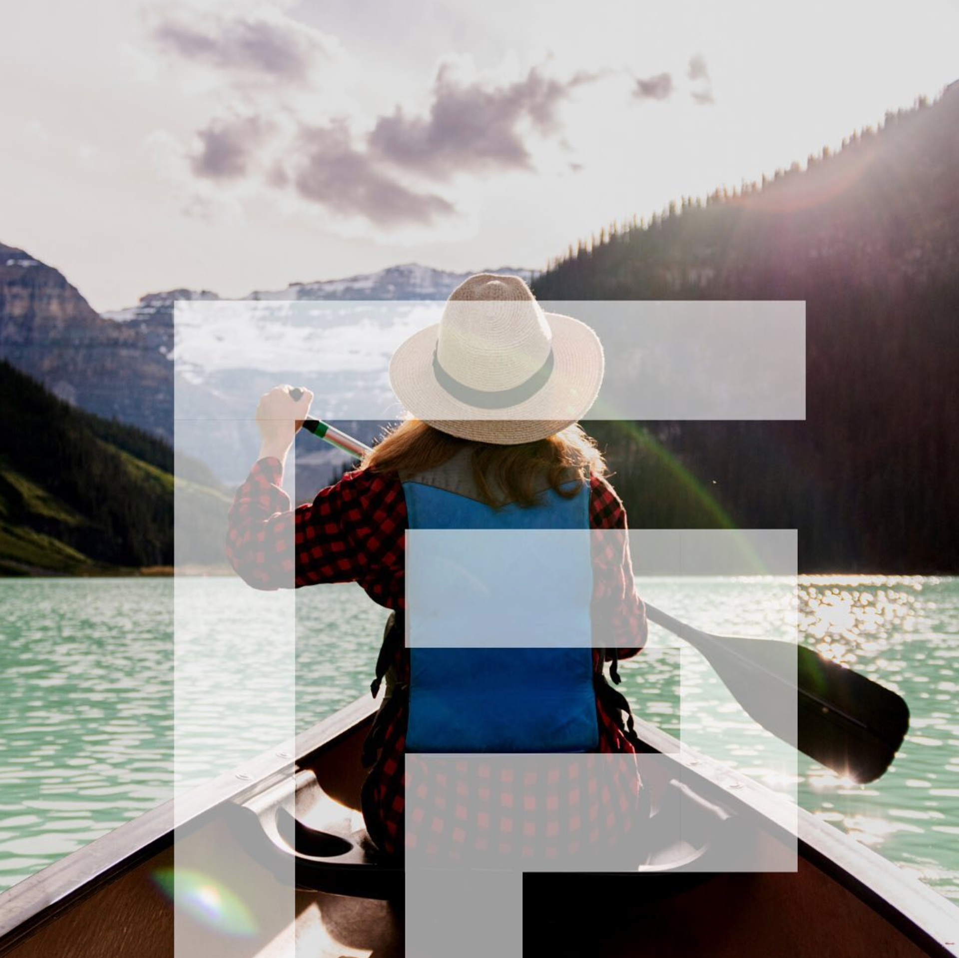 Person in a hat canoeing on a lake, mountain backdrop, holding paddle.