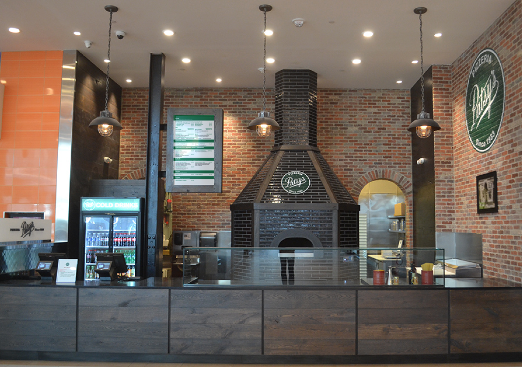 Interior of a pizza restaurant with a brick oven and wooden counter.