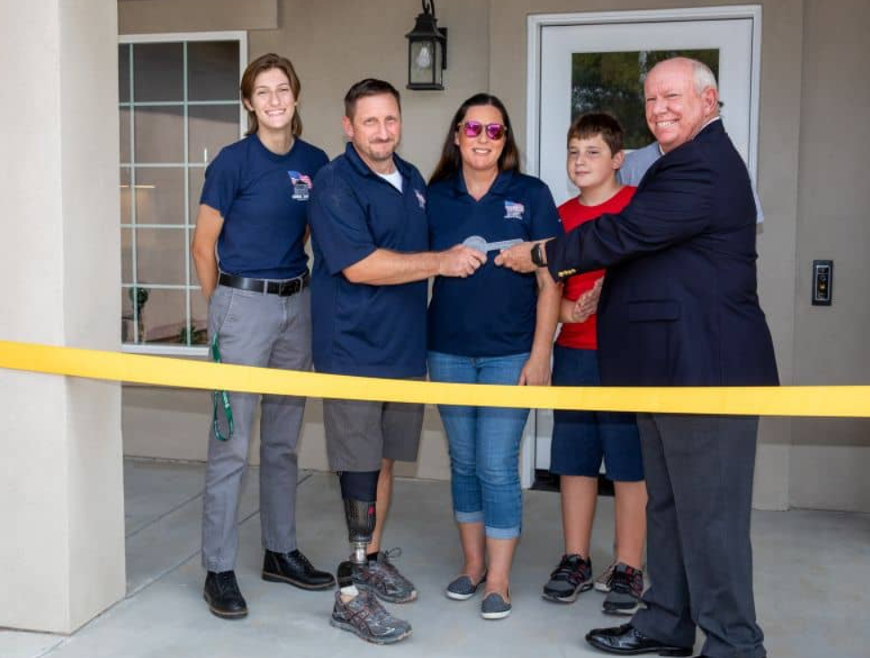 A family receives keys from a man at a house-warming ribbon cutting event.