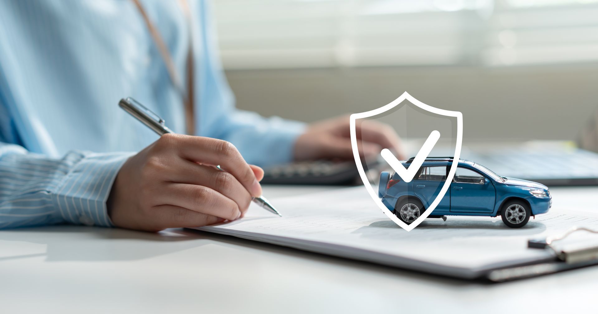 Person signing auto insurance documents beside model car and protection shield.