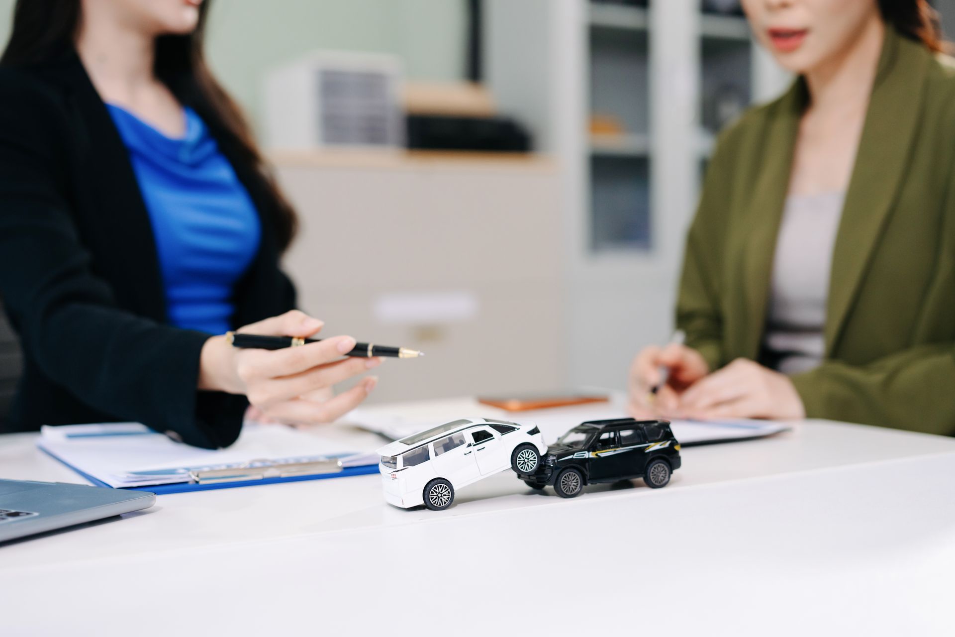 Agent and client discussing an auto insurance policy claim with toy cars in a collision Agent and client discussing an auto insurance policy claim with toy cars in a collision
