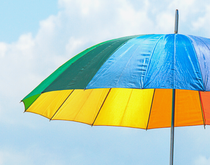 Rainbow umbrella against a partly cloudy blue sky.