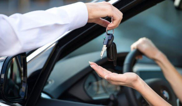 Person handing car keys to another person in a car.