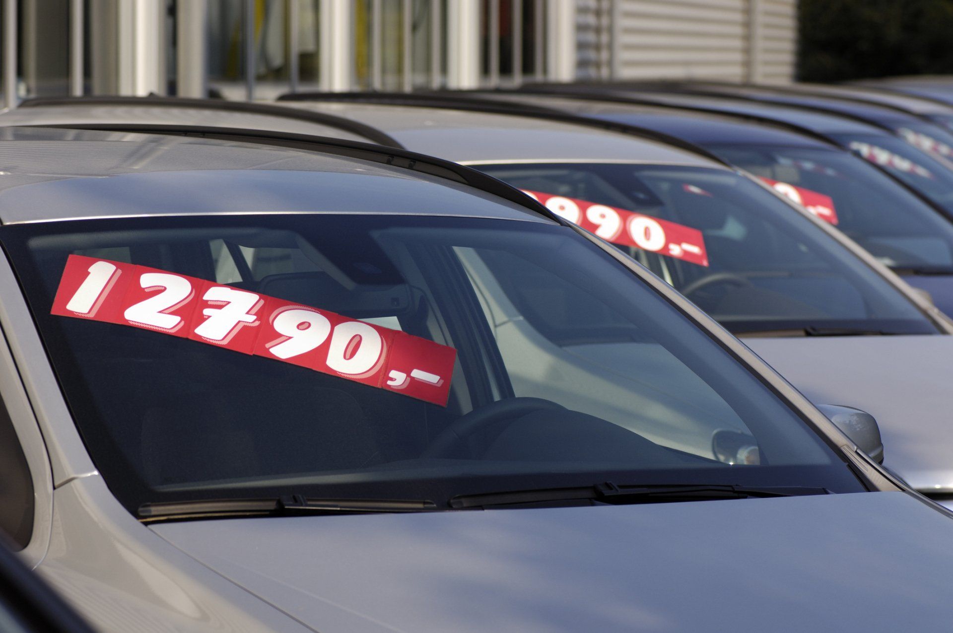 Cars lined up at a dealership with red price tags visible on windshields; focus on the front car, showing a price of 12790.