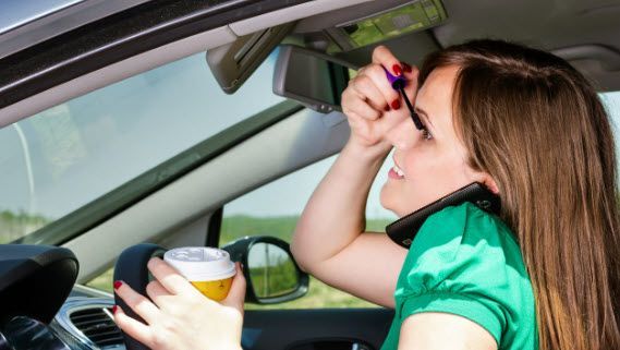 Woman applying makeup, talking on phone, and holding coffee while driving car.