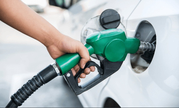 Hand fueling a white car with a green gas pump at a gas station.