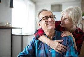 Elderly couple embracing; woman with arms around man smiling, both in plaid shirts.