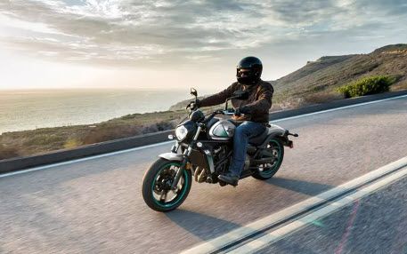 Motorcyclist on black bike rides along coastal road. Setting sun, sea, and mountains.