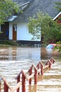 Flooded street in front of houses; red fence partially submerged. A car is partially underwater.