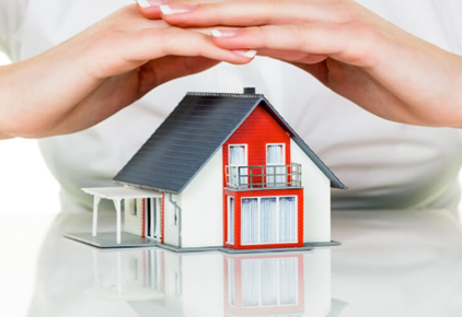 Hands protect a miniature house, symbolizing home security and insurance.