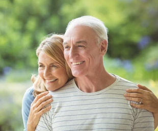 Smiling older couple embracing outdoors; woman's arms around man.
