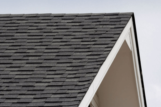 Close-up of a dark gray shingle roof against a light gray sky, with a white-trimmed gable end.