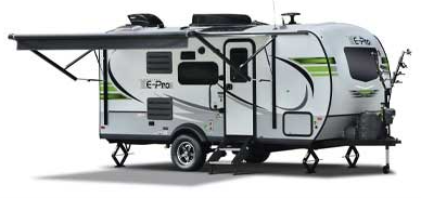 A compact, white and green travel trailer with an awning extended, set on a sunny day.