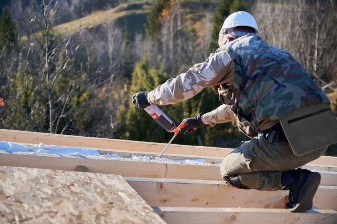 Construction worker securing wood framing with a red tool on a roof under construction