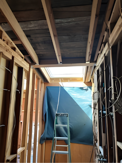 Ladder in a framed interior under renovation, with blue tarp covering the far wall and exposed ceiling beams.