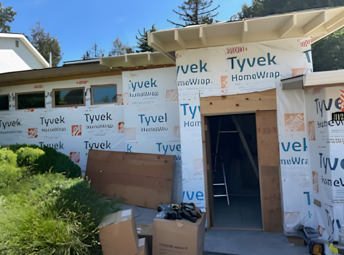 Partially built house wrapped in Tyvek, with an open doorway and construction materials outside