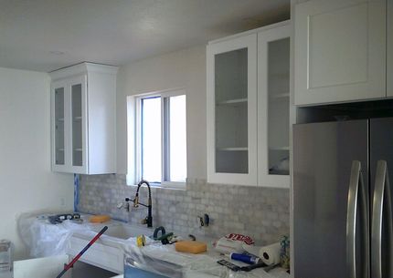 Modern kitchen under renovation with white cabinets, tiled backsplash, and tools on the counter