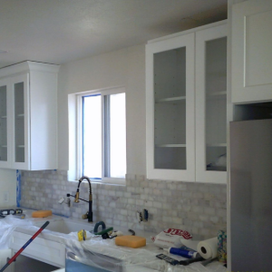 Kitchen under renovation with white cabinets, tiled backsplash, and sink covered in plastic and tools