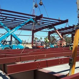 Construction workers assembling a red steel building frame with a blue lift under a clear sky