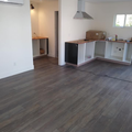 Empty unfurnished room with gray wood flooring, white walls, and a kitchen counter area with pendant light