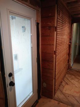 Wooden hallway with a frosted glass door and a herringbone wood floor, leading into a rustic interior.