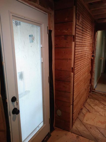 Wooden hallway with a frosted glass door and a herringbone wood floor, leading into a rustic interior.