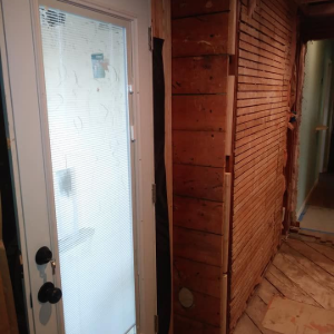 Interior hallway with white door, wood-paneled wall, and tiled floor under renovation