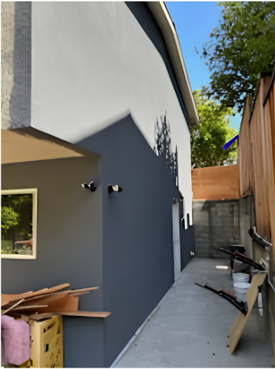 Narrow outdoor side yard beside a gray house, with scattered boards and a fence at the end.