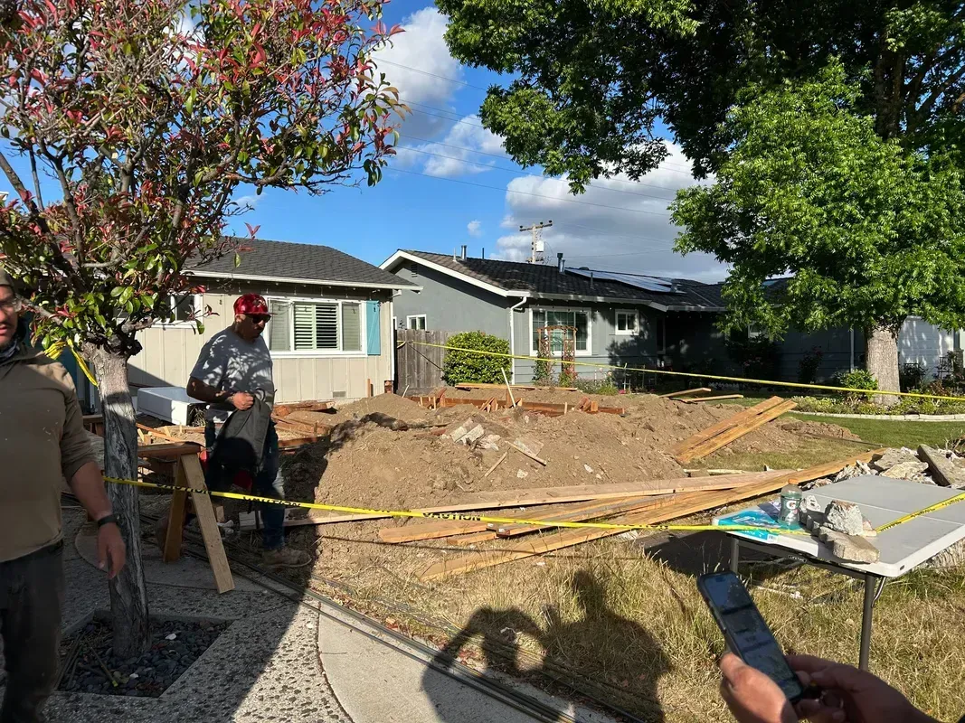 Construction workers near a damaged house with a collapsed yard and caution tape