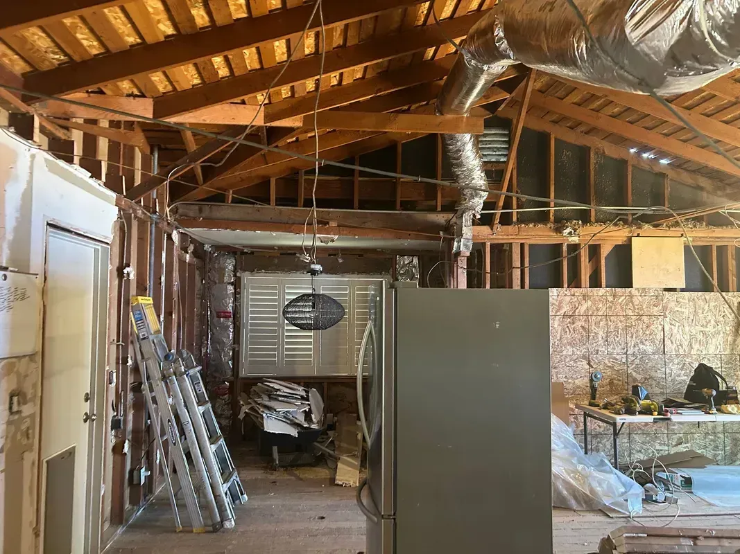 Partially furnished unfinished attic with exposed rafters, insulation, ladders, and stored items
