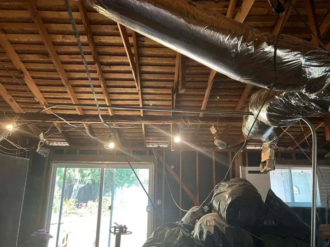 Exposed attic ceiling with insulation, ductwork, and sunlight through window openings in a partially finished room