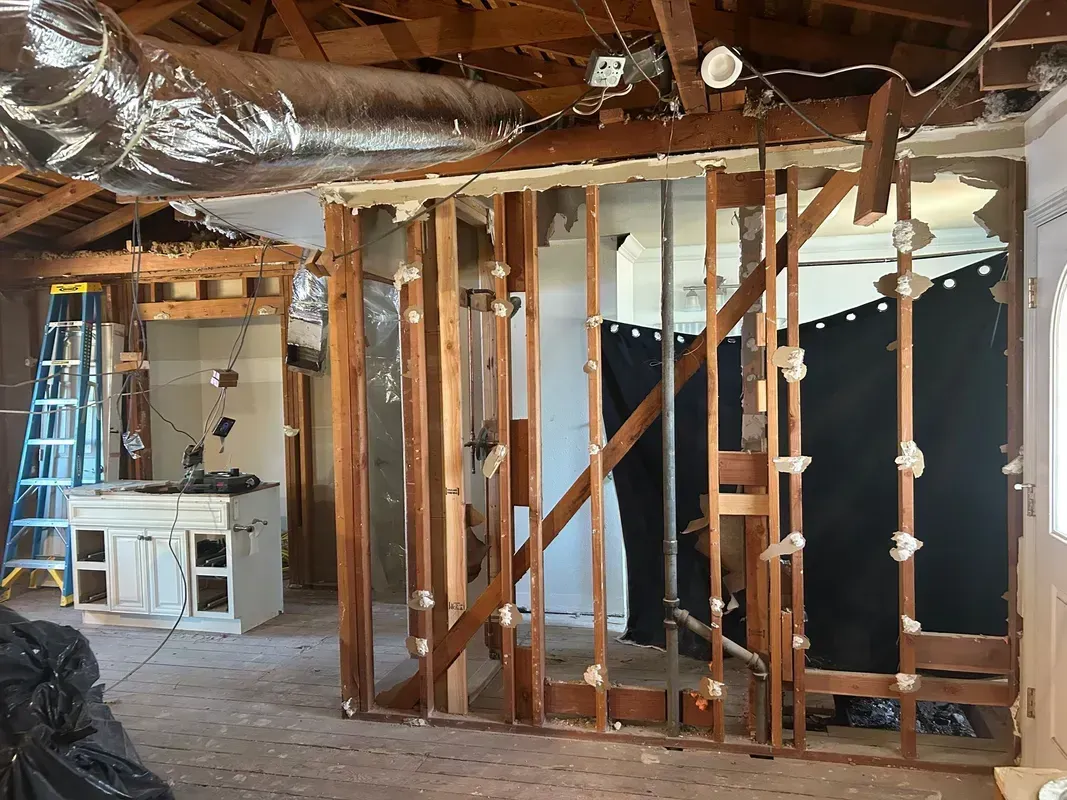 Partially demolished room with exposed wooden studs, debris, and a ladder during renovation.
