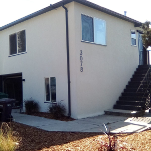 Two-story beige house with exterior staircase, windows, and the number 3078 on the wall