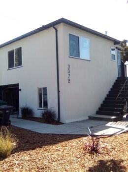 Two-story beige house with exterior stairs and small yard with mulch and plants