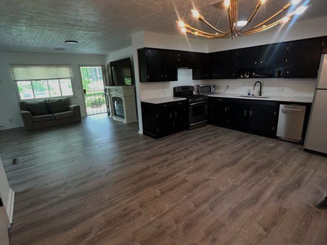 Open kitchen and living room with dark cabinets, gray wood floors, and a large windowed seating area