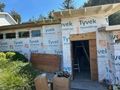 Partially built house exterior wrapped in Tyvek with an open doorway and construction materials nearby