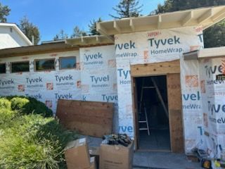 Partially built house exterior wrapped in Tyvek with an open doorway and construction materials nearby